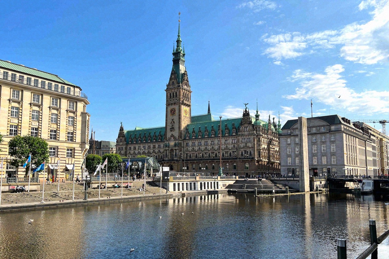 Blick über den Alsterfleet auf das prächtige Hamburger Rathaus mit seinem markanten Turm, im Sonnenschein unter blauem Himmel